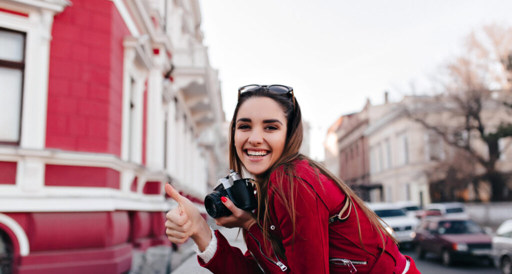 enthusiastic female photographer with red manicure relaxing in weekend. outdoor portrait of fashionable girl with camera having fun in city..